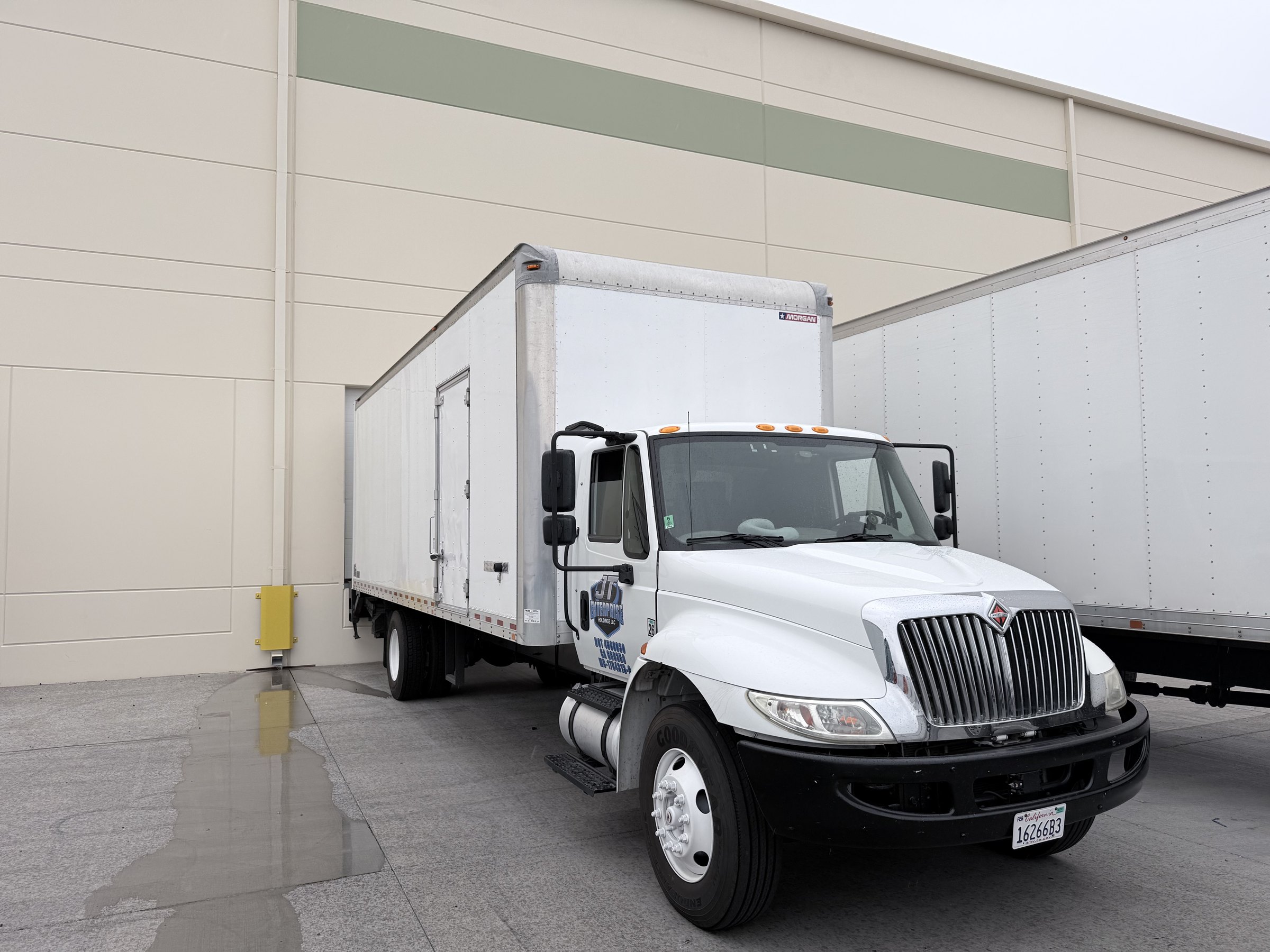 JT Enterprise Holdings 26-foot International straight truck at a warehouse during wet weather